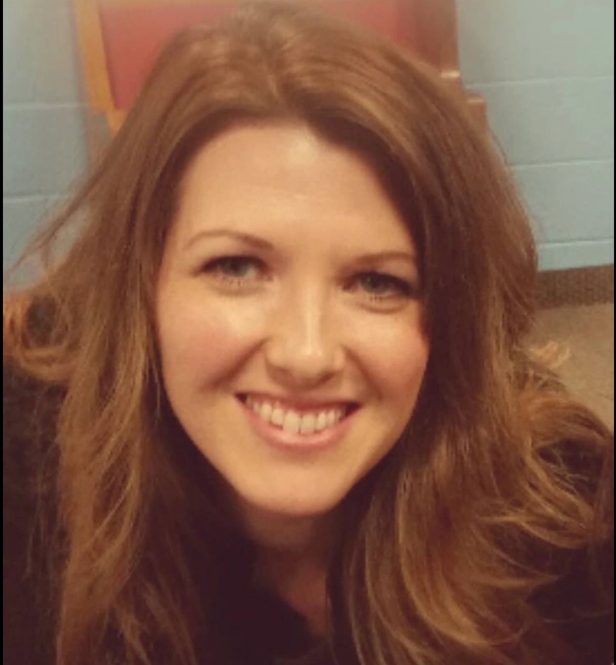 Smiling woman with long brown hair indoors.