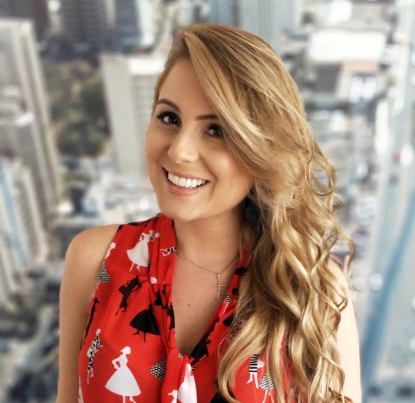 Smiling woman with long blonde hair wearing a red dress with black and white silhouettes.