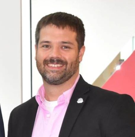 Smiling man in a black blazer and pink shirt.